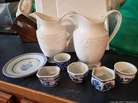 Group photo showing two white ceramic pitchers, five small blue and white porcelain planters or votive holders, and one porcelain plate with blue decoration.