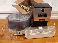 Photo showing Cuisinart coffee maker, food dehydrator with trays, box of canning jars and the electric yogurt maker jars in front.