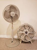 Photo of the two fans side by side against white wall, showing standing house fan and floor wind machine fan.