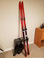 Full view of the Kastle skis standing upright on the floor with Technica ski boots placed below them showing overall condition and size.