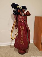 Full view of vintage red Spalding golf bag with golf clubs inside, showing knitted club headcovers and leather-like exterior