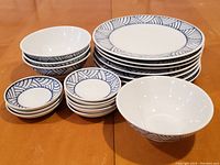 Porcelain plates, bowls, and small dishes arranged on a wooden table, showing the blue geometric pattern around the edges and quantity.