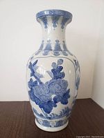 Full view of tall blue and white porcelain vase showing floral and decorative motifs on the body, neck, and rim.