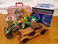 Image showing the grouping of vintage toys on a wooden table including the K'NEX race car, Cabbage Patch Dogs suitcase with a toy horse, Hoberman globe box, wooden car, bucket of toys, and box of crayons.