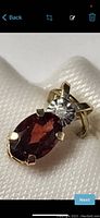 Angled close-up of pendant showing oval garnet and round diamond in gold setting