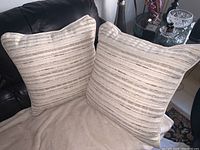 Two beige striped square accent pillows placed on a couch showing their front sides.