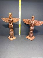 Two totem poles side by side showing overall appearance and relative heights. Yellow measuring tape in background.