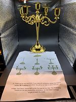 Fully assembled brass-colored candelabra standing approximately 11 inches tall with printed assembly instructions placed beneath it.