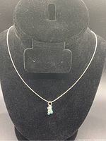 Full view of necklace displayed on a black bust stand showing the silver chain and teddy bear pendant with blue accents.