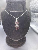 Full view of the garnet pendant shown hanging on a black jewelry display stand with the chain.
