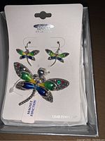 Set of dragonfly earrings and magnetic brooch on white display card showing colorful enamel and metal detailing