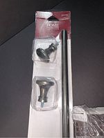 Photo showing two black decorative finials and part of the silver metal rod in packaging