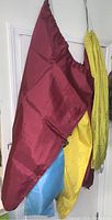 Side view photo of different colored laundry bags hanging, showing burgundy, blue, and yellow bags with drawstring closures.