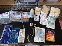 Top view showing laid out first aid supplies including gauze pads, adhesive pads, scissors, tape rolls, antiseptic bottle and hot/cold packs.
