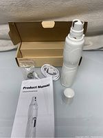 Pet nail grinder with USB cable, extra grinding stone in plastic bag, product manual, and original open cardboard box.