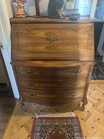 Front view of wooden secretary desk closed showing ornate metal handles, curved drawers, and cabriole legs.