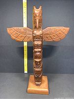 Front view of totem pole on base with measuring tape indicating height.