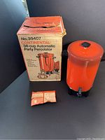 Orange coffee percolator with original box and instruction leaflet, showing front and side view.