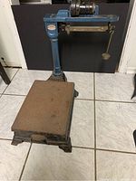 Full side view of the vintage scale showing the rusted platform, heavy base, blue painted column and top beam structure with cast iron weights mounted on top