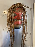 Front view showing carved face with red and black paint and cedar bark hair