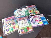 Five window decorating kits shown together, four in original sealed packaging and one opened, displayed on a black surface in a corner.