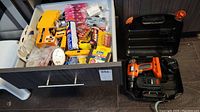 Drawer containing assorted household hardware, Dewalt drill bits, batteries, and various small items in plastic bags and packaging.
