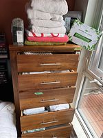 Stack of multiple white, pink, and olive green towels on a wooden drawer unit.