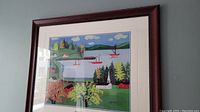 Framed art print of colorful folk art coastal scene with boats, trees, houses, and hills.