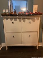 Front view of white wooden shoe rack with shoes on top, four drop-down compartments shown closed.