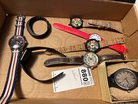 Box containing eight watches including Guess, Garmin Vivosmart band, Ferrari-themed watches, a leather band watch and a black band watch in box.