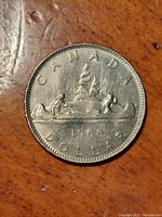 Reverse side of a 1968 Canadian one dollar voyageur coin showing the canoe scene with voyageur and aboriginal paddling, northern lights, date, face value, and 'CANADA' inscription.