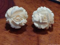 Close-up of both handcrafted floral earrings showing detailed petal carving in off-white material.