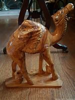 Front and left side view of the handcrafted wooden dromedary camel sculpture on a rectangular base, showing one hump and two small pots at the feet.