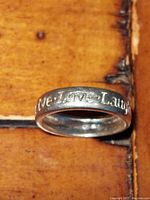Ring placed on a wooden surface showing the inscription 'Live Love Laugh' engraved on the band.