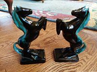 Pair of black and turquoise stallion bookends on wooden floor, showing overall shape and appearance.