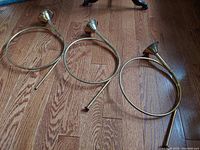 Three vintage brass decorative French horns arranged on wooden floor. Two have mouthpieces, one is missing mouthpiece.