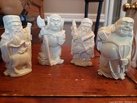 Four vintage cultured ivory-colored Lucky Gods figurines on wooden surface, showing full group and details