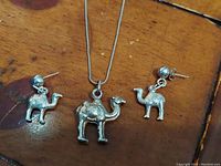 Group photo of vintage Italian solid sterling silver camel necklace with pendant and matching earrings on wooden surface