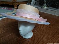 Photo of vintage woven summer hat with pink ribbon and lace detail displayed on white mannequin head, showing side angle and decorative bow.