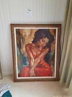 Framed oil painting on board depicting a seated woman in a red dress, displayed against a wall