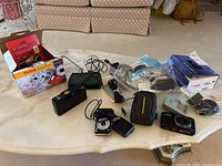 Lot overview with all three cameras, accessories such as cases, cables, charger, and original packaging displayed on a table.