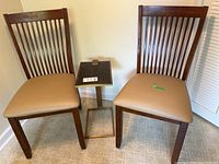 Two wooden chairs with beige seats and small metal frame side table arranged together on linoleum floor against wall.