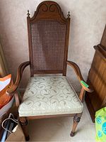 Wooden dining armchair with cane woven back and light cushioned seat, showing front view with curved armrests and slight scratches