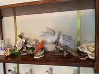 Shelf display showing multiple ceramic birds and white Capodimonte style flower branches.
