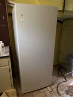 Front view of a white Frigidaire upright freezer standing on a tiled floor next to cabinets.