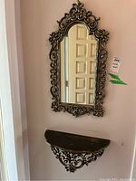 Front view of ornate framed mirror above matching wall shelf attached to wall