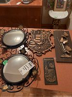 Two round mirrors with ornamental black metal frames and three metal art plaques on red tabletop.