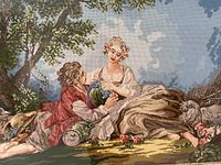 Close-up of the full needlepoint showing a romantic countryside scene with a man and woman reclining and sheep nearby.