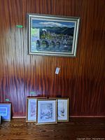 Framed needlepoint artwork hung on wall above three framed prints leaning against wall