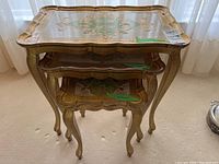 Front view of three nested gold-painted tables showing scalloped tops and cabriole legs